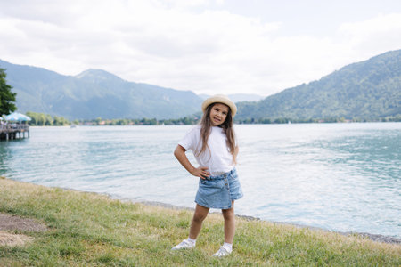 Adorable little girl in denim skirt white t-shirt and Panama straw stand in front of big beautiful lake. High quality photoの写真素材