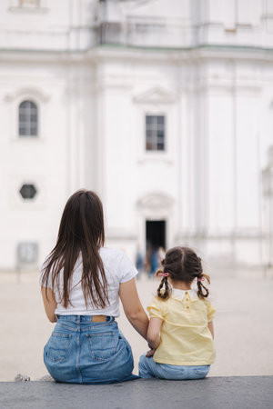 Back view of little girl sits with her mom on stone bench outdoorの写真素材