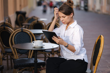 Business lady working outdoor on terrace in cafe using tablet. Female freelancerの写真素材