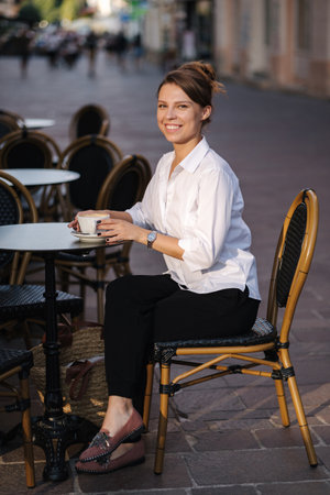 Happy smiled woman drinking coffee on terrace in cafe. Female in white shirt have rest during the breakの写真素材