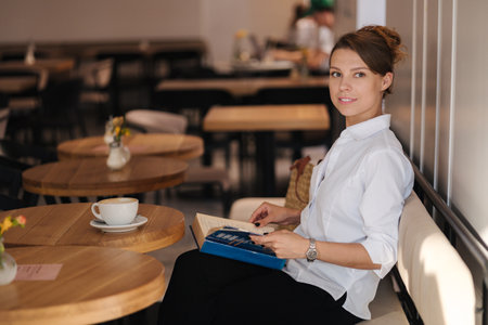 Side view of woman reading book in cafeの写真素材