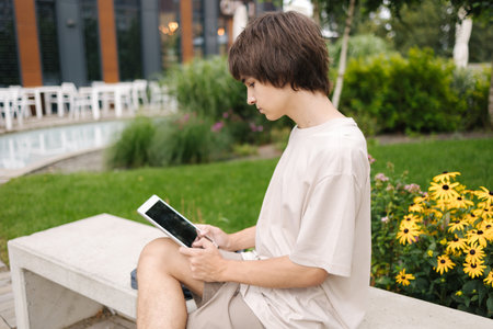 Teenage boy using tablet outdoors. Happy student have rest during the break in park near the campusの写真素材