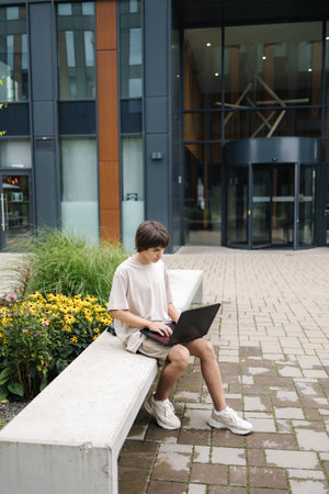 Teenage boy study outdoors. Male sitting on a bench under a house in a residential areaの写真素材