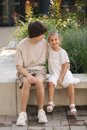 Adorable little girl sitting on bench with her teenage brotherの写真素材