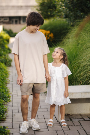 Adorable little girl walking in the park with her teenage brother. Happy kids look to each otherの写真素材