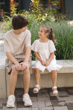 Adorable little girl sitting on bench with her teenage brother. Look to each otherの写真素材