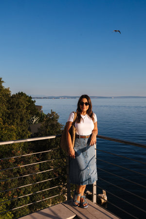 Portrait of woman standing on height balcony in front of sea landscape. Beautiful bird in sky. Sunset timeの写真素材