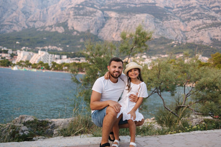 Adorable little daughter with her lovely father. Portrait of happy family in front of mountains and seaの写真素材