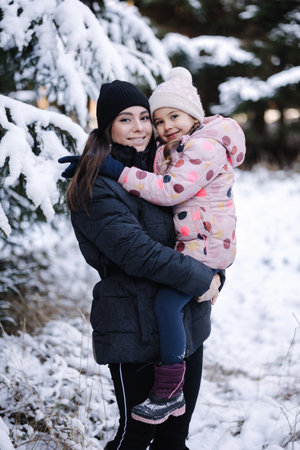 Beautiful young mom hug her adorable little daughter in snowy forest. Happy familyの写真素材