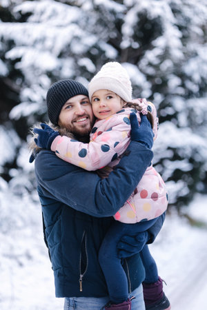 Portrait of happy dad with his beautiful little girl in snowy forest. Happy family time at Christmas holidaysの写真素材