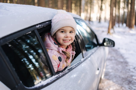 Adorable little girl looks out of the car window and looks at the beautiful snowy forestの写真素材