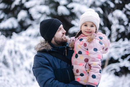 Portrait of happy dad with his beautiful little girl in snowy forest. Happy family time at Christmas holidaysの写真素材