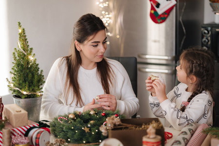 Mom and daughter making Christmas wreath using fresh pine branches and festive decorations. Christmas moodの写真素材