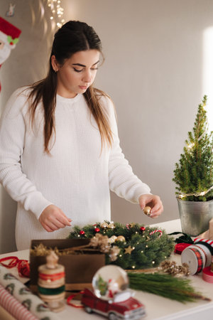 Attractive woman making Christmas wreath using fresh pine branches and festive decorations. Christmas moodの写真素材