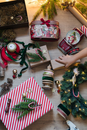 Top view of little girl take Christmas present. Decorating and preparing for winter Hollidays. Wreath, wrapping paper bows and other detailsの写真素材