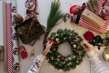 Top view of mom and daughter decorating Christmas wreath. Process of home made winter decorの写真素材