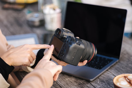 Close-up of photographer holding mirrorless camera and checking pictures. Women points a finger at the cameraの写真素材