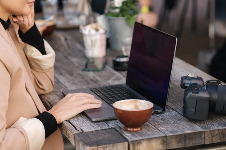 Side view of woman working on laptop in cafe outdoors. Stylisch freelancer drink coffee