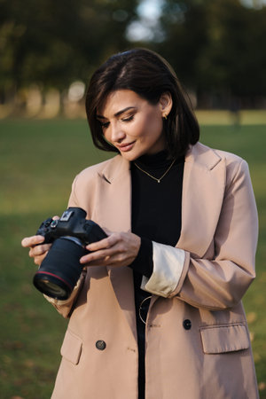 Portrait of professional woman photographer with DSLR camera walking in the park. Stylish female...