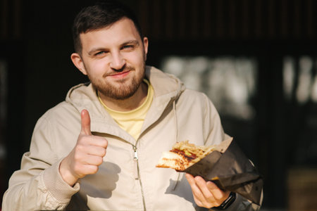 Handsome man having traditional hot dog cuisine during rest break. Caucasian guy enjoying street cuisine outdoor. Male eating unhealthy fast food.の写真素材