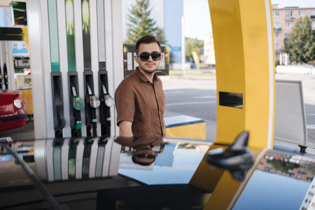 Handsome man refuelling his luxury car on self service gas station. Filling benzine at gasoline fuel...