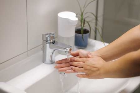 Female washing hands in bathroom sink at home checking temperature touching running water with handの写真素材