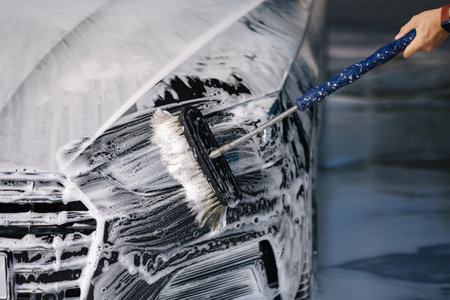 Man washes a car using a special brush at a car wash. Close up of man wash left headlight. The car is in foamの写真素材