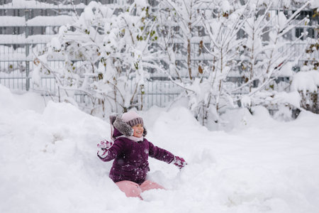 Little girl wearing a cozy winter outfit, happily exploring deep snow. The pure white snow surrounds...