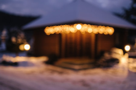 Blurred view of a cozy log cabin with glowing Christmas lights, surrounded by snow, creating a warm holiday ambiance.の写真素材
