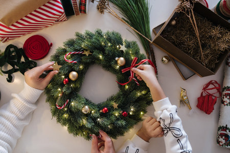 Top view of mom and daughter decorating Christmas wreath. Process of home made winter decorの写真素材