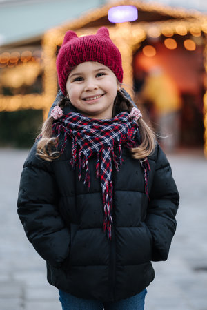 Portrait of adorable little girl standing in front of Christmas lights in old town. Background of bokehの写真素材