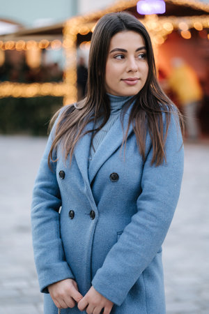 Portrait of happy beautiful female in blue winter coat standing in front of Christmas light in old town. Winter moodの写真素材