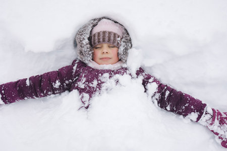 Adorable little girl bundled up in winter clothes, playing in a snowy wonderland. She stands joyfully among snow-covered trees, capturing the magic of a snowy day.の写真素材