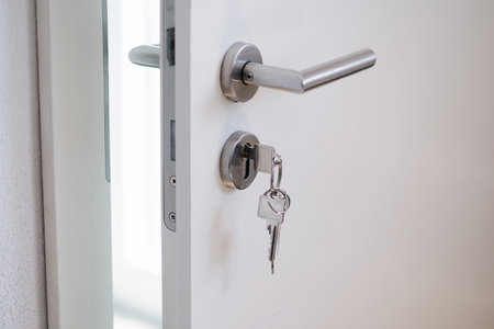 Silver keys hanging in a modern door lock with a stainless steel handle, close-up view. The door is openの写真素材
