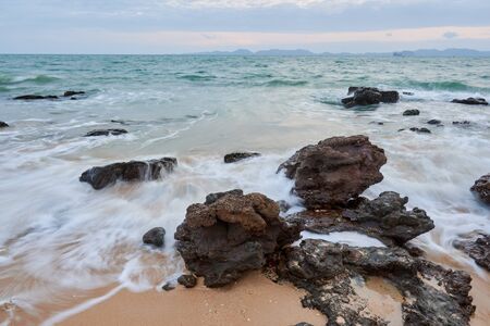 a wavy sea with rocks near a beach.の写真素材