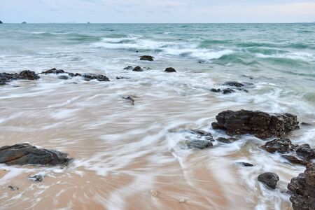 a wavy sea with rocks near a beach.の写真素材