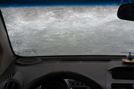 Interior view of a car with frosted windshield obscuring visibility, highlighting winter driving...