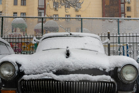 Car partially covered with fresh snow after winter snowfall. Cold weather conditions, urban winter scene, frozen vehicle surface and snowy texture. Transportation and seasonal weather conceptの写真素材