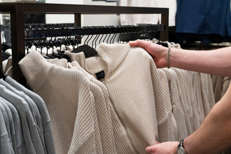 Male hand selecting clothing from a rack in a retail store. Customer choosing apparel in a modern...
