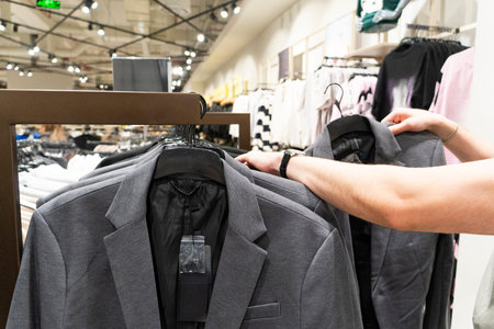 Male hand selecting clothing from a rack in a retail store. Customer choosing apparel in a modern...