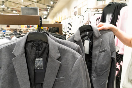 Male hand selecting clothing from a rack in a retail store. Customer choosing apparel in a modern...