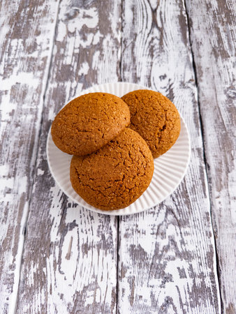 Three homemade oatmeal cookies on white plate over rustic wooden background. Fresh baked sweet...