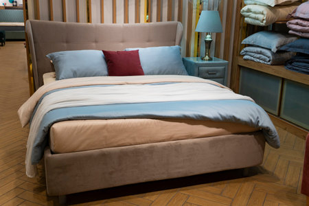 Showroom bedroom setup featuring upholstered bed with pastel bedding, pillows, nightstand, lamp, and shelving unit with folded linensの写真素材