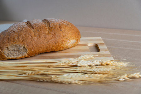 Fresh homemade bread loaf on a wooden cutting board with wheat ears on a wooden table. Natural...