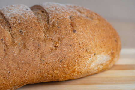 Fresh homemade bread loaf on a wooden cutting board with wheat ears on a wooden table. Natural...