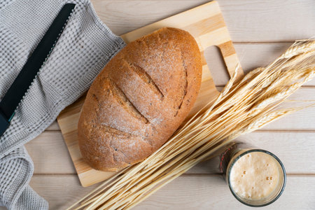 Round rustic bread loaf with flour crust placed beside a glass of kvass, complemented by wheat...