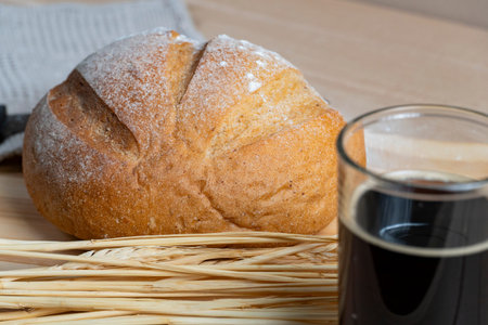 Round rustic bread loaf with flour crust placed beside a glass of kvass, complemented by wheat...