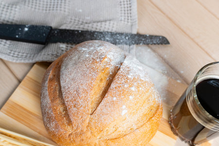 Round rustic bread loaf with flour crust placed beside a glass of kvass, complemented by wheat...