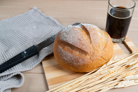 Round rustic bread loaf with flour crust placed beside a glass of kvass, complemented by wheat...