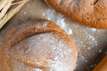 Two artisan bread loaves rest on parchment with wheat stalks and rolling pin, creating a cozy...
